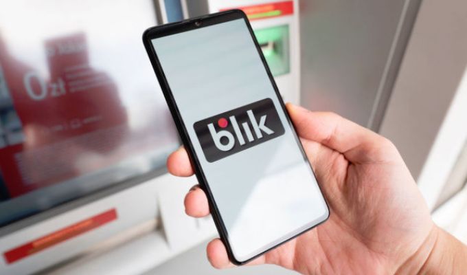 Zdjęcie przedstawiające dłoń trzymającą telefon komórkowy na którego ekrani widoczne jest duże logo BLIKw dłoni